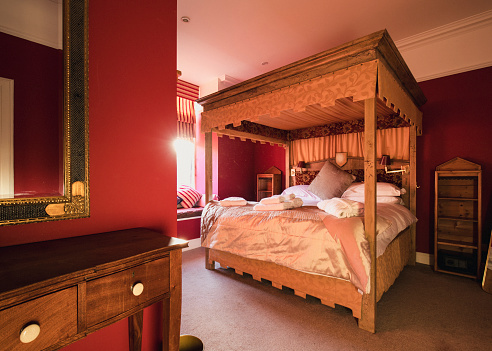 A bedroom in a luxury hotel with red walls and double canopy bed.