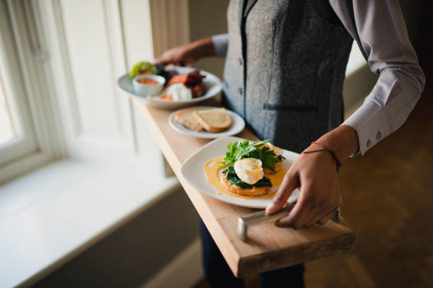 Delicious Room Service A waiter is standing while holding a breakfast tray with a full English breakfast and poached eggs on toast covered in Hollandaise sauce on it. room service stock pictures, royalty-free photos & images