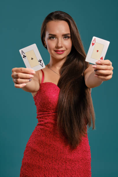 brunette girl with a long hair, wearing a sexy red dress is posing holding two playing cards in her hands, blue background - smiling casino human hand beautiful imagens e fotografias de stock