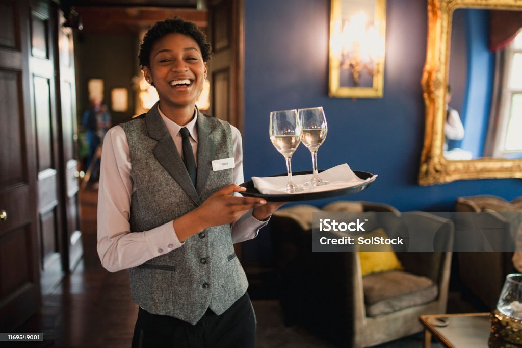 I Love My Job! A well-dressed waitress is laughing and enjoying being at work, while she is holding wine glasses to be served to guests. Hotel Stock Photo