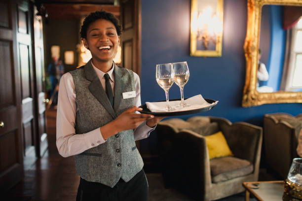 I Love My Job! A well-dressed waitress is laughing and enjoying being at work, while she is holding wine glasses to be served to guests. concierge photos stock pictures, royalty-free photos & images
