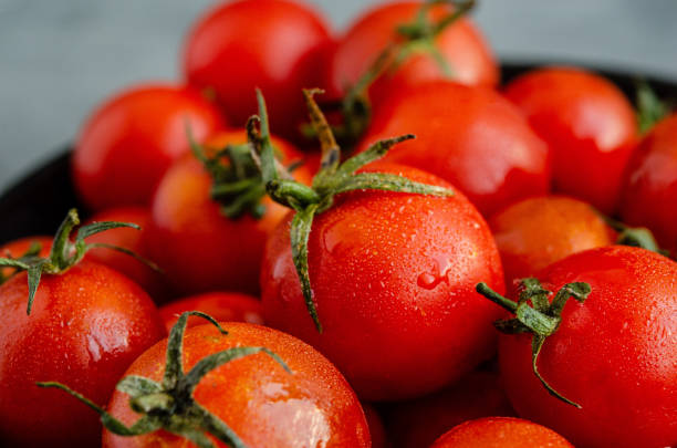 istock Red cherry tomatoes with water droplets in a black ceramic plate close-up on a dark concrete background. 1169549045