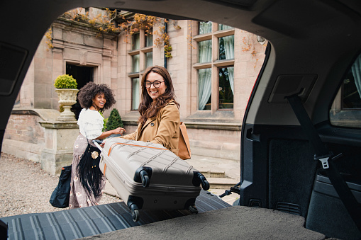 Two friends arrive at a luxury hotel where they are unloading their suitcases from their car trunk.