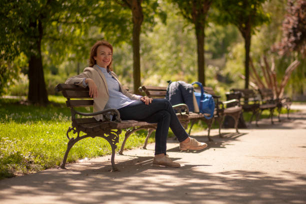 istock one young lady, sitting in park on a bench, relaxing on a beautiful Spring day. 1169552362