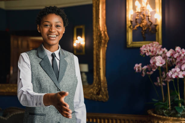 A Warm Welcome A happy female hotel employee is standing with her arm outstretched, ready to shake hands with guests. porter photos stock pictures, royalty-free photos & images