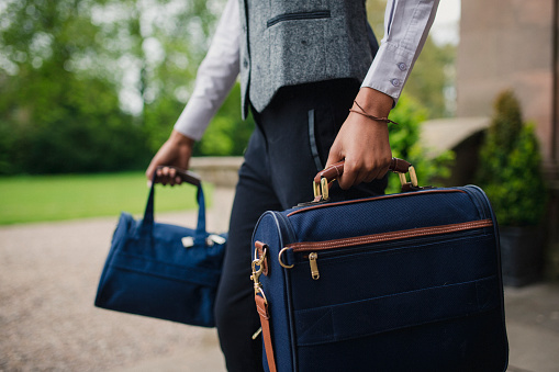 A close up of an unrecognisable hotel porter is carrying two suitcases.