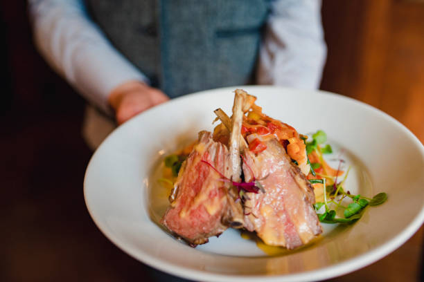 An unrecognisable waiter holding a lamb dish.