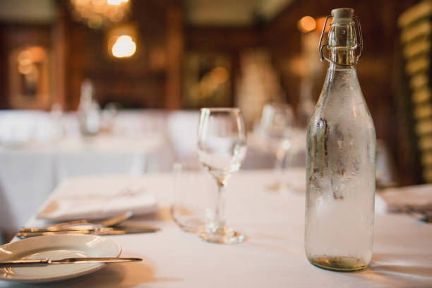 Table at a Restaurant A close up shot of some drinking glasses and a water bottle with cutlery and serving dishes on a table in a restaurant. bottled water on table stock pictures, royalty-free photos & images