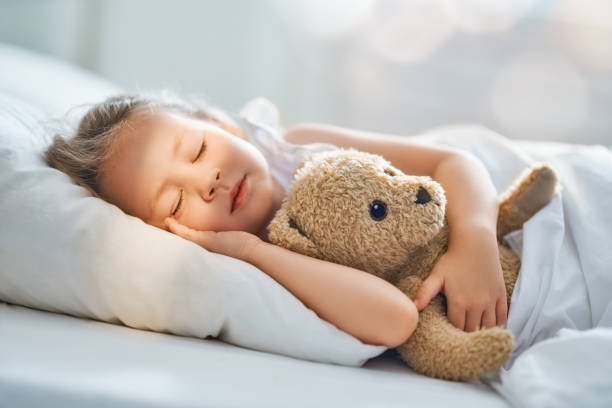 child is sleeping in the bed Adorable little child is sleeping in the bed with her toy. The girl is hugging the teddy bear. stuffed toy stock pictures, royalty-free photos & images