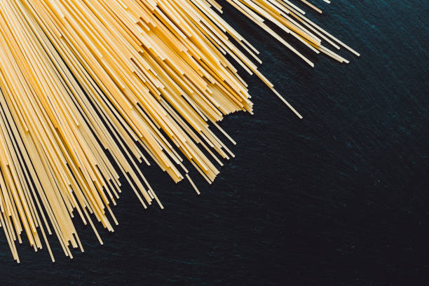 mazzo di spaghetti in fila sulla parte superiore di un tavolo nero come sfondo - italian cuisine dry pasta directly above foto e immagini stock