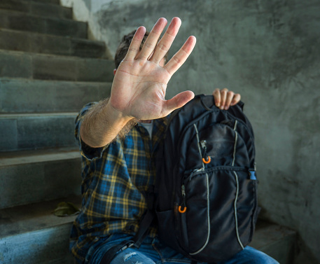 stop bullying abuse and discrimination campaign. young student man with backpack rasing hands covering his face helpless suffering harassment and violence due to sexual orientation