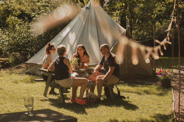 Family Glamping Weekend Looking through defocused stringed twinkle lights to a family sitting at a picnic bench while enjoying an alcoholic beverage. cumbria photos stock pictures, royalty-free photos & images