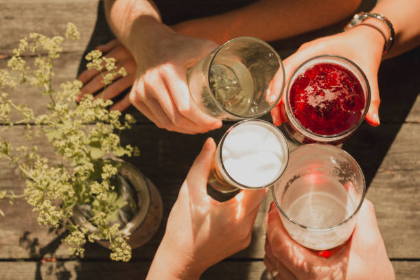 Cheers! High angle view of four unrecognisable people making a celebratory toast with alcohol while sitting outdoors in the sun light. pub table top view stock pictures, royalty-free photos & images