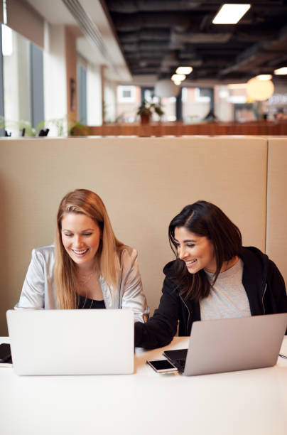 Two Young Businesswomen In Meeting Around Table In Modern Open Plan Workspace