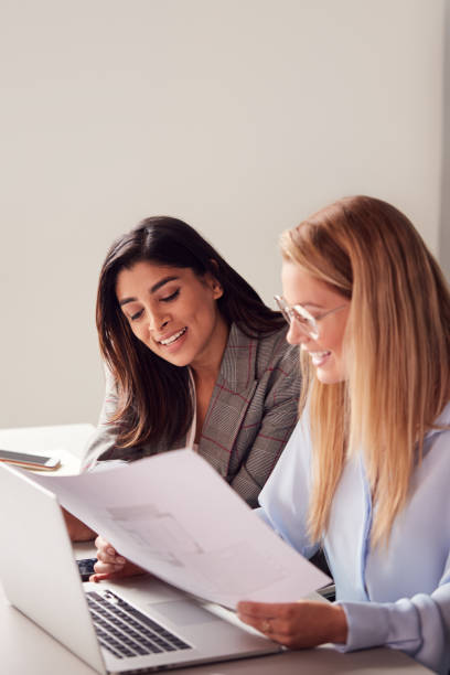 istock Two Young Businesswomen In Meeting Around Table In Modern Workspace Discussing Documents 1169563312
