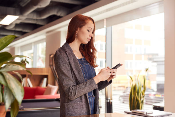 istock Casually Dressed Young Businesswoman Checking Mobile Phone In Modern Open Plan Workplace 1169563389