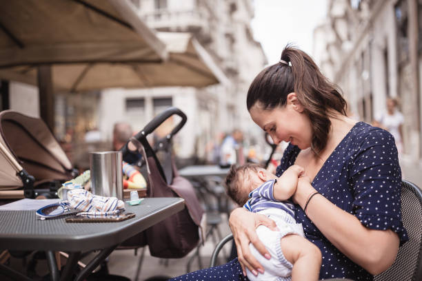 giovane madre che allatta il suo bambino in luogo pubblico - baby mother summer park foto e immagini stock