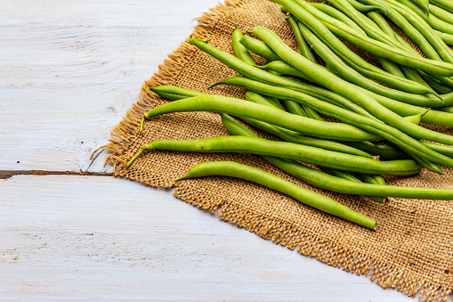 Phaseolus vulgaris, green common bean or kidney bean on rustic sackcloth. Harvest organic vegetables as a fresh ingredient for cooking healthy food. Wooden boards background, copy space, close up