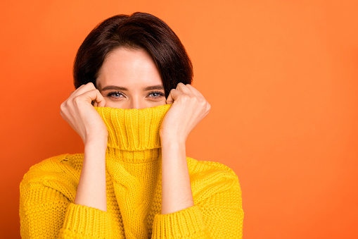 Close up photo of cute nice, charming girl hiding from cold by wrapping up in collar while isolated with orange background