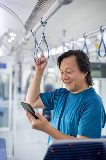 istock Mature Asian man is looking at his mobile phone in subway train 1169590075