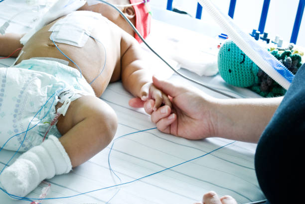main réconfortant un bébé malade avec le syndrome de down accroché à un ventilateur dans un service de soins intensifs d'hôpital - opération du coeur photos et images de collection