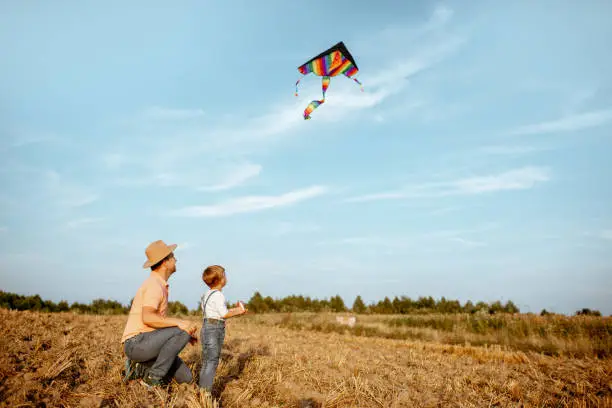 Father with son launching colorful air kite on the field. Concept of a happy family having fun during the summer activity