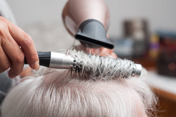 hands of hairdresser on old woman with gray hairs - hairdresser at home concept stock photo