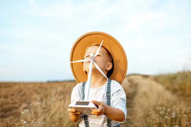 Portrait of a curious young boy playing with toy wind turbine in the field, studying how green energy works from a young age