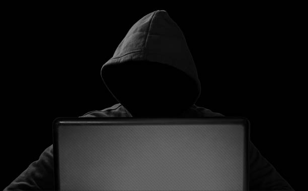 istock hacker with glowing mask behind notebook laptop in front of isolated black background internet cyber hack attack concept 1169602137