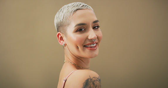 Studio portrait of an attractive young woman with piercings posing against a brown background