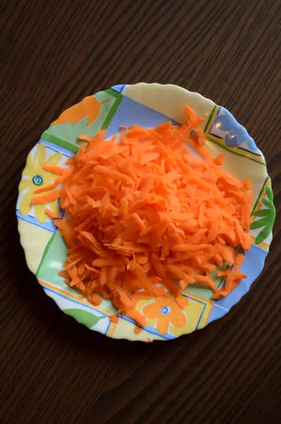 Grated carrots in a small colorful plate on the wooden table