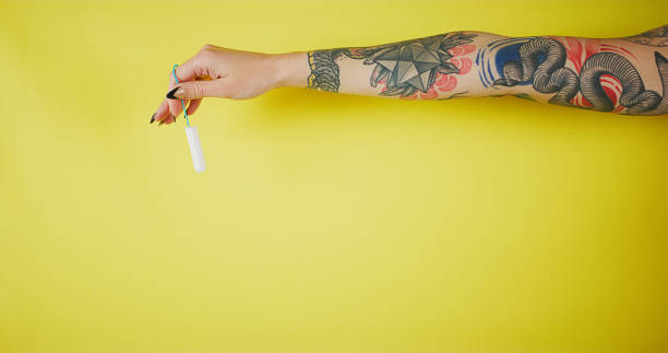 The tiniest product with the biggest benefit Studio shot of an unrecognizable woman holding a tampon against yellow background tattoo arm stock pictures, royalty-free photos & images