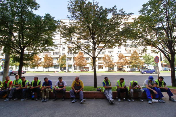 Bucharest, Romania - September 10, 2018: Several construction workers are relaxing sitting on a curb while smoking or drinking coffee or soft drinks during lunch break in Bucharest.