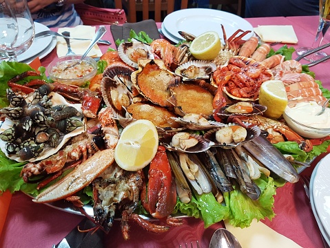 HORIZONTAL IMAGE, FIRST FLAT OF MARISCO VARIADO, MARISCADA GALLEGA, HOT, COOKED, READY TO EAT. IT'S ON THE TABLE WITH THE WHITE DISH AND RED TABLET. CONTAINS ALL THE DRESS AND SAUCES NEEDED TO DRESS THE TASTE OF EACH ONE. DELICACY. DELI. DELICACY