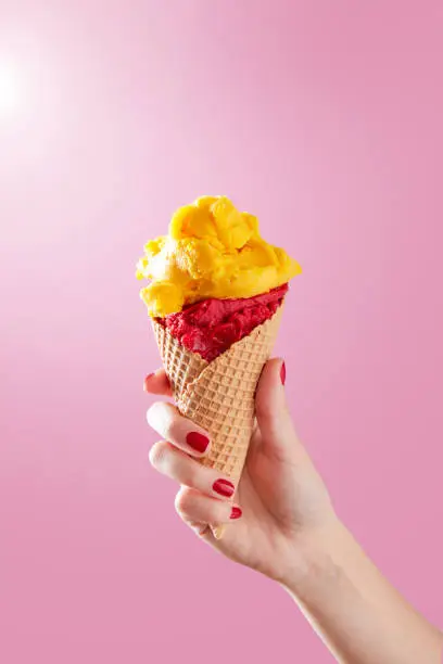 Photo of Woman hand holding ice cream cone on a pink background. Copy space