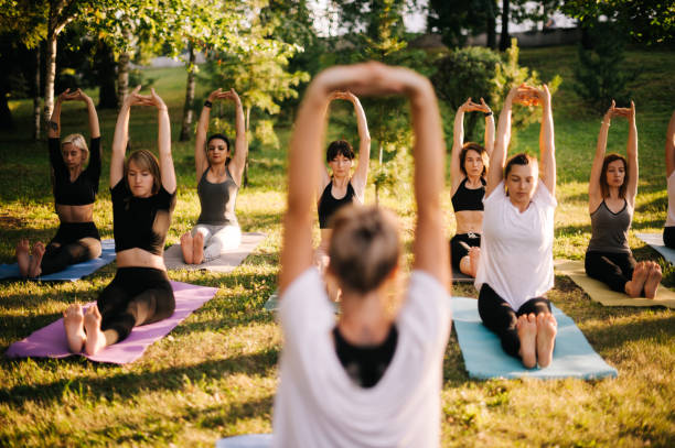 groupe de femmes pratiquent le yoga et s'assied avec des mains vers le haut le matin dans le stationnement de ville - yoga class caucasian young adult group of people photos et images de collection