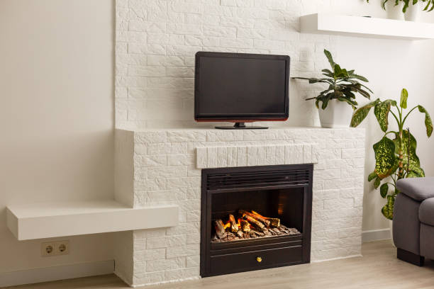 habitación de estilo moderno. hay un televisor en la pared blanca, estante blanco con una flor en flor, tv remota, decoraciones en una forma de chimenea negra - home decorating living room luxury fireplace fotografías e imágenes de stock