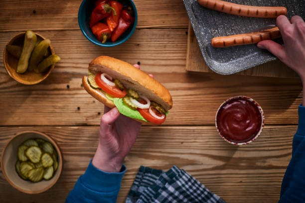 Making hot dog with cucumber, lettuce, tomato, onion and cheese