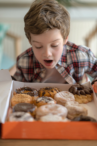 Surprised little boy looking at a variety of donuts in box ready to eat - Lifestyles