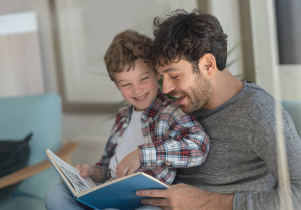 istock Excited daddy and son having fun laughing while reading a book at home 1169630818