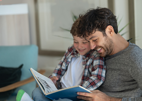 Loving daddy and son reading a book together having fun laughing and smiling