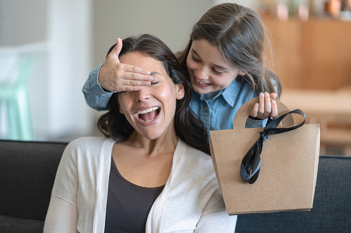 Beautiful little girl surprising her mom with a gift for mother's day both smiling