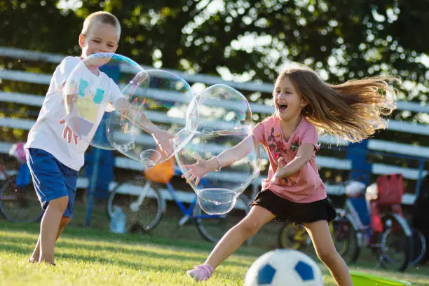 Playful happy children are playing with giant soap bubbles outdoors, cheerful childhood.