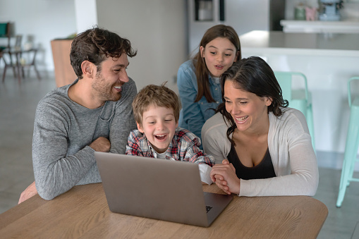 Happy family having fun using a laptop at home laughing and smiling