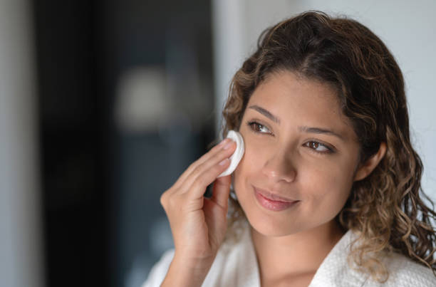 Beautiful woman cleaning her face with a cotton pad Portrait of a beautiful woman cleaning her face with a cotton pad in the bathroom â beauty concepts facial cleanser stock pictures, royalty-free photos & images