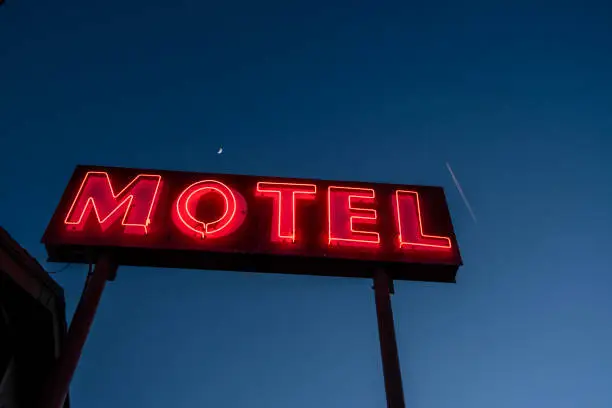 Photo of illuminated neon motel sign red letters dark blue sky
