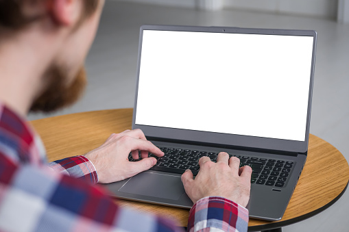Hombre estudiante escribiendo en el teclado gris de la computadora portátil con la pantalla blanca en blanco photo