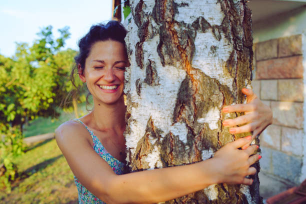 Young woman in summer dress hugging embracing tree trunk in her backyard in spring autumn fall day enjoying nature joyful happy smiling hug Young woman in summer dress hugging embracing tree trunk in her backyard in spring autumn fall day enjoying nature joyful happy smiling hug hugging tree stock pictures, royalty-free photos & images