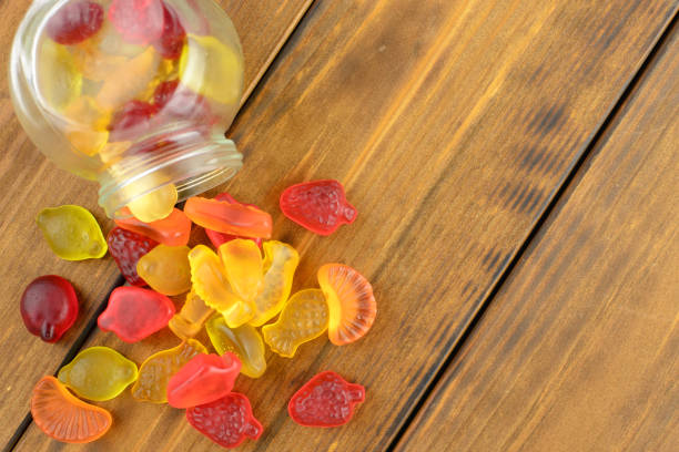 Colored gummy fruit candy spilled, on a brown wooden table Colored gummy fruit candy spilled, on a brown wooden table gum drop photos stock pictures, royalty-free photos & images