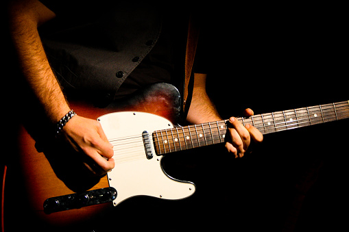 Musician dots in a telecaster fender during a concert in the dark, only a spotlight illuminates the guitar